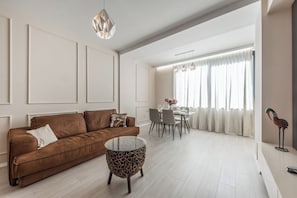 A modern living room with a brown sofa, a glass coffee table, and a dining area with a white table and chairs. - Luxury Block District Apartment (Tirana)