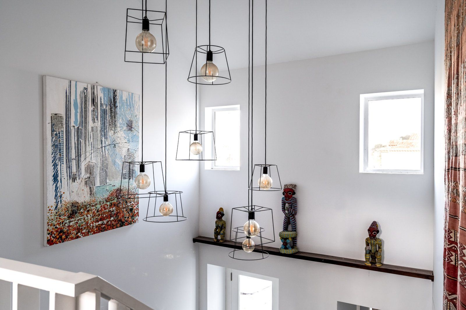 A modern interior with multiple hanging pendant lights, a large abstract painting, and a shelf with decorative items.