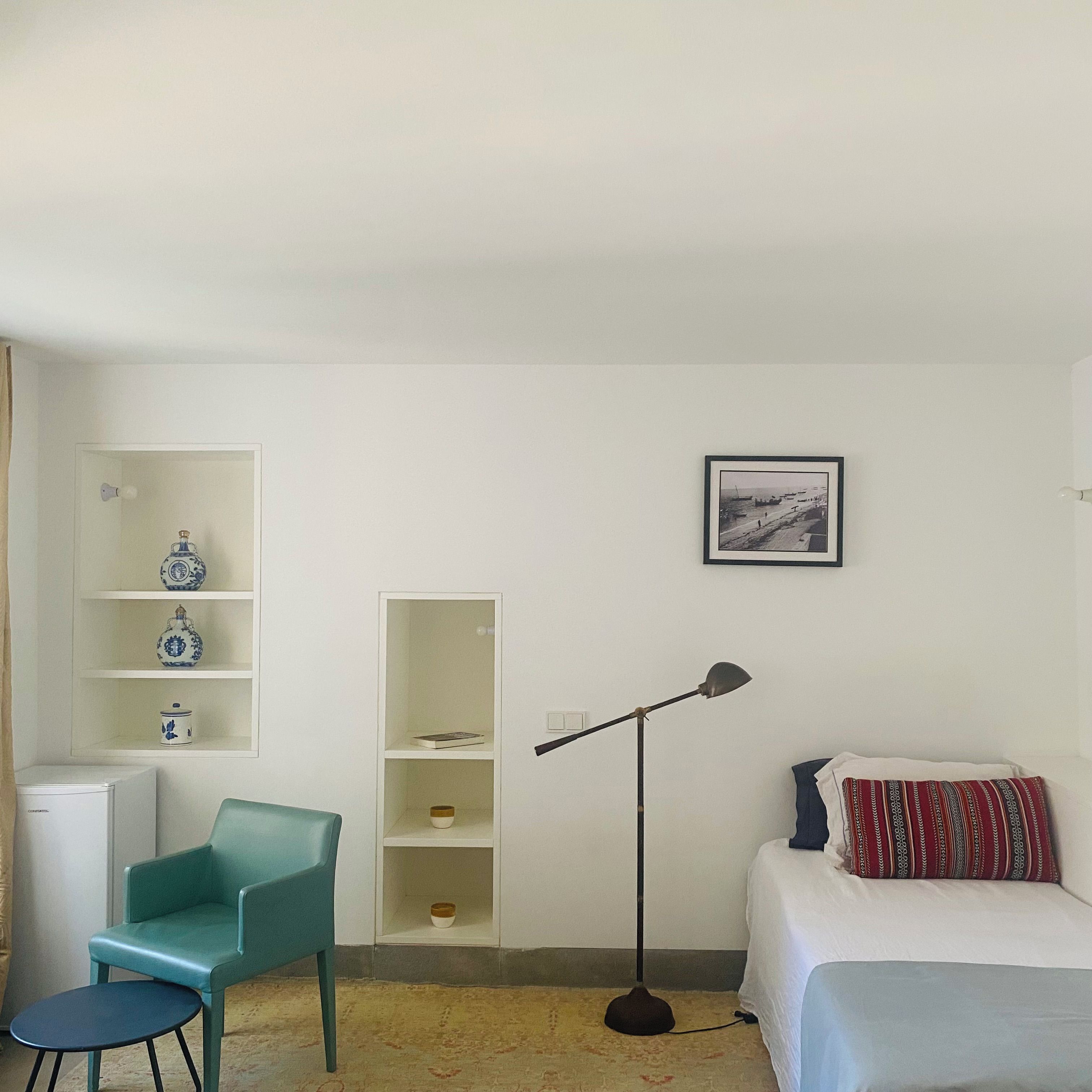 A bedroom with a bed, a desk, a chair, a bookshelf, a floor lamp, and a framed picture on the wall.
