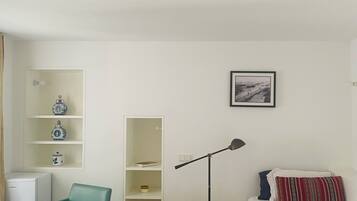 A bedroom with a bed, a desk, a chair, a bookshelf, a floor lamp, and a framed picture on the wall.