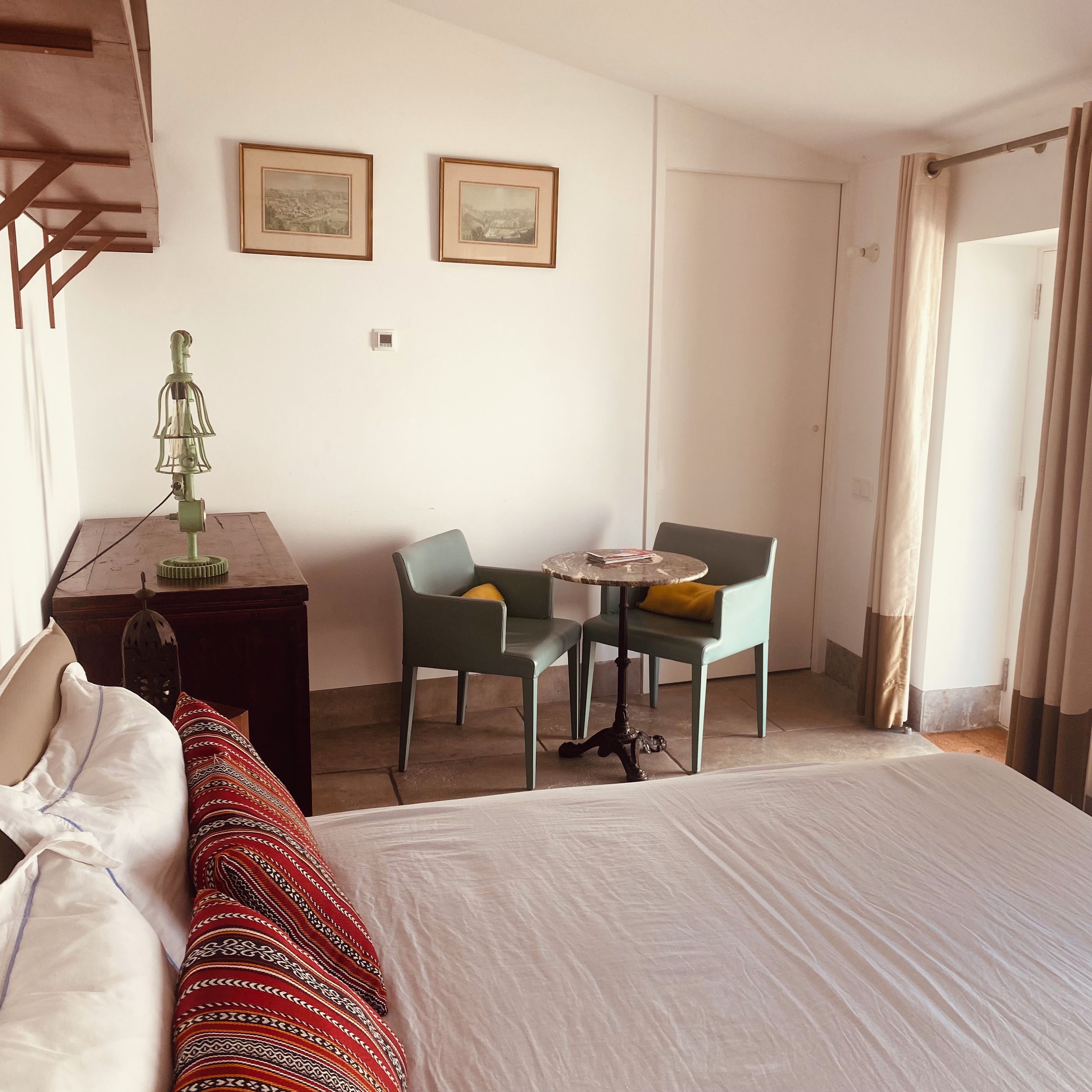 Une chambre d’hôtel avec un lit, un bureau doté d’une lampe, deux chaises disposées autour d’une petite table et deux tableaux encadrés accrochés au mur.