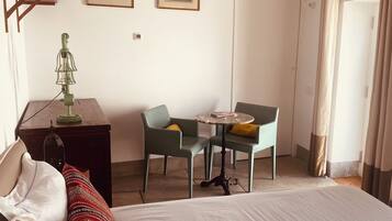 Une chambre d’hôtel avec un lit, un bureau doté d’une lampe, deux chaises disposées autour d’une petite table et deux tableaux encadrés accrochés au mur.