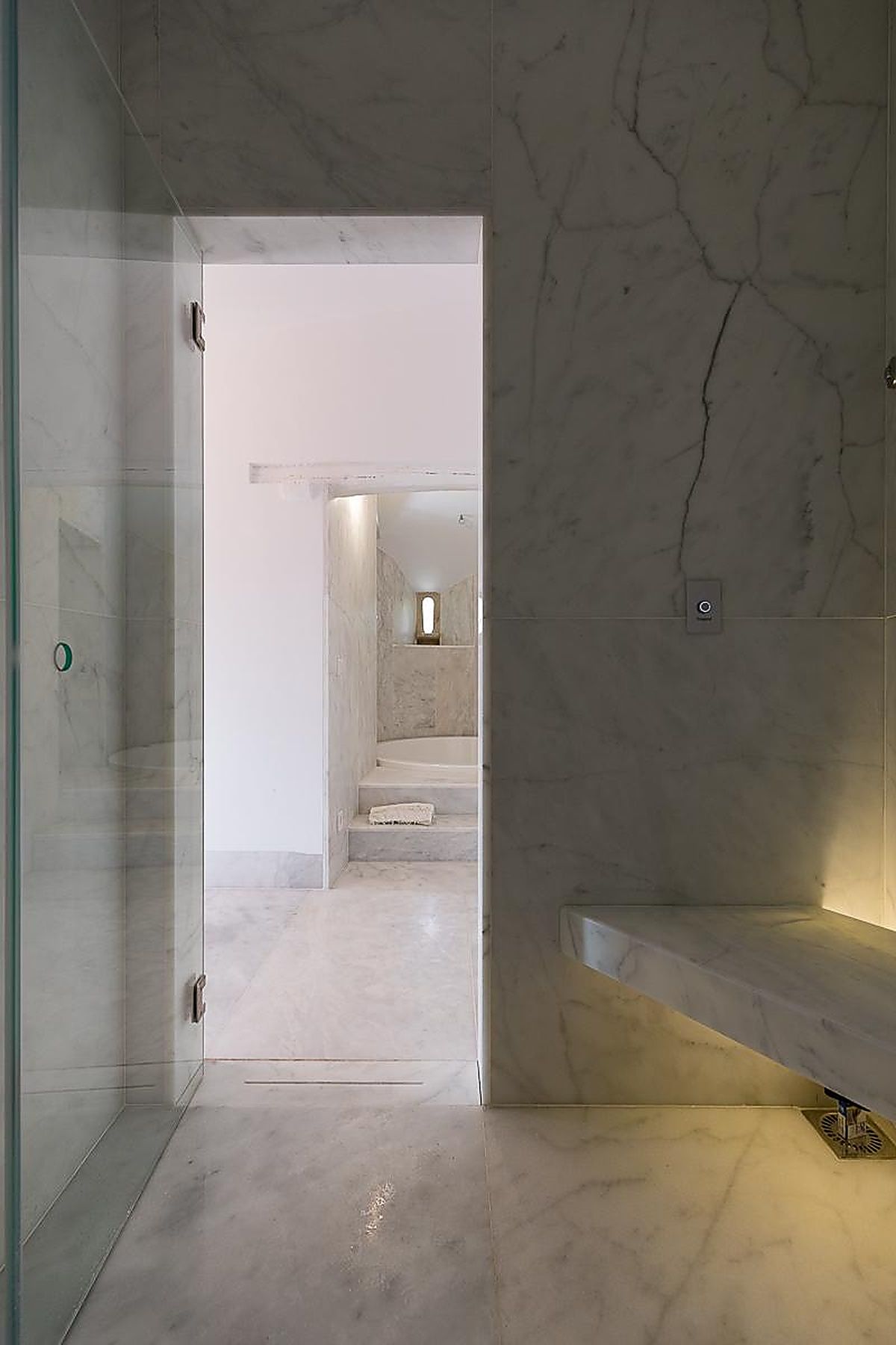 A modern interior with a marble floor, a glass door, and a staircase leading to a room with a window.