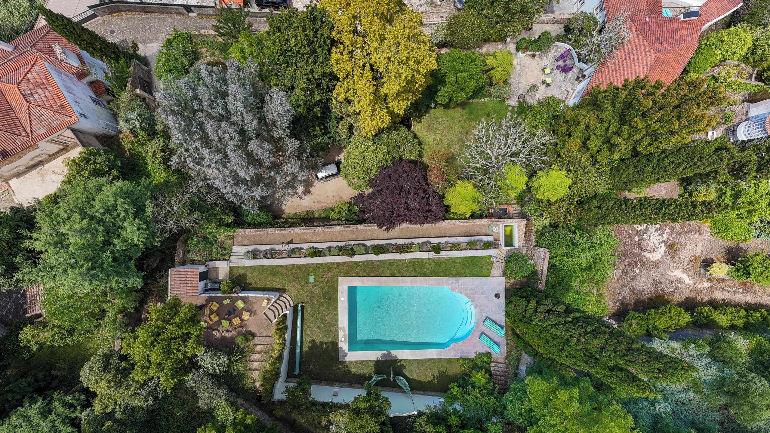 Vue aérienne d’une propriété dotée d’une piscine, d’un espace patio aménagé avec des sièges, ainsi que de divers arbres et arbustes.