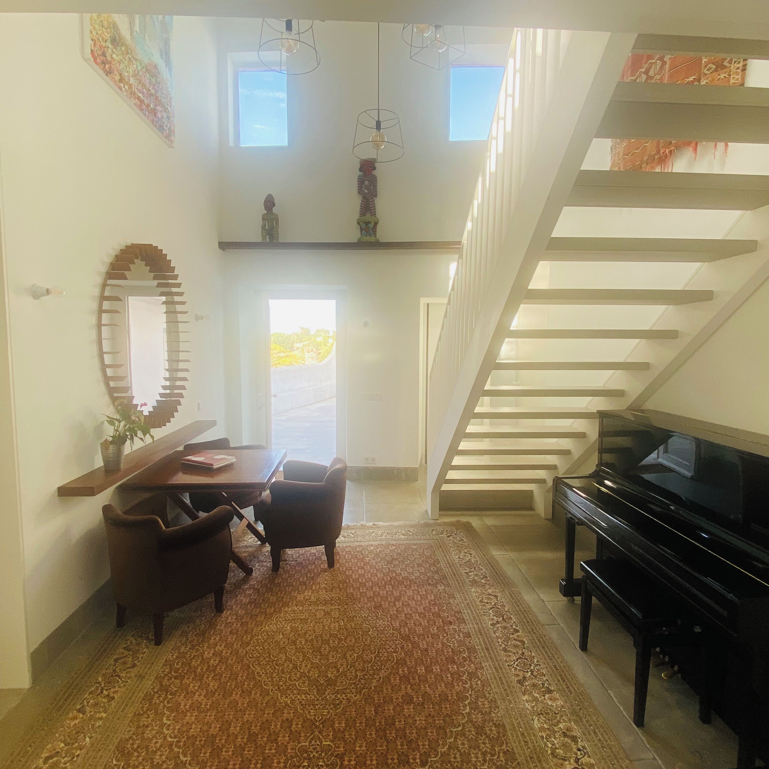 A spacious living area with a piano, a dining table with chairs, a large mirror, and a staircase.