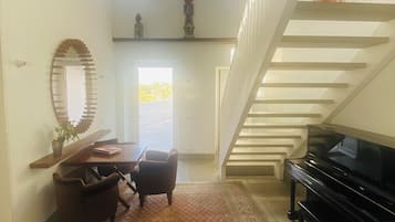 A spacious living area with a piano, a dining table with chairs, a large mirror, and a staircase.