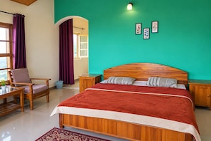 A bedroom with a wooden bed, a chair, a small table, a window with curtains, and a green wall. - Leela Orchard Sonapani (Mukteshwar)