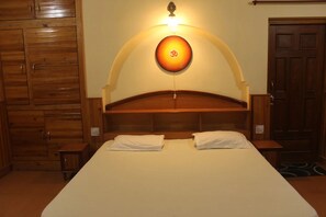 A bedroom with a large bed, wooden headboard, two bedside tables, and a wall-mounted light fixture. - Leela Orchard Sonapani (Mukteshwar)