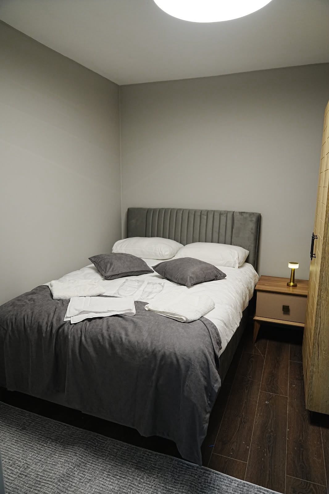 Un dormitorio con cama, almohadas, una mesita de noche y una lámpara.