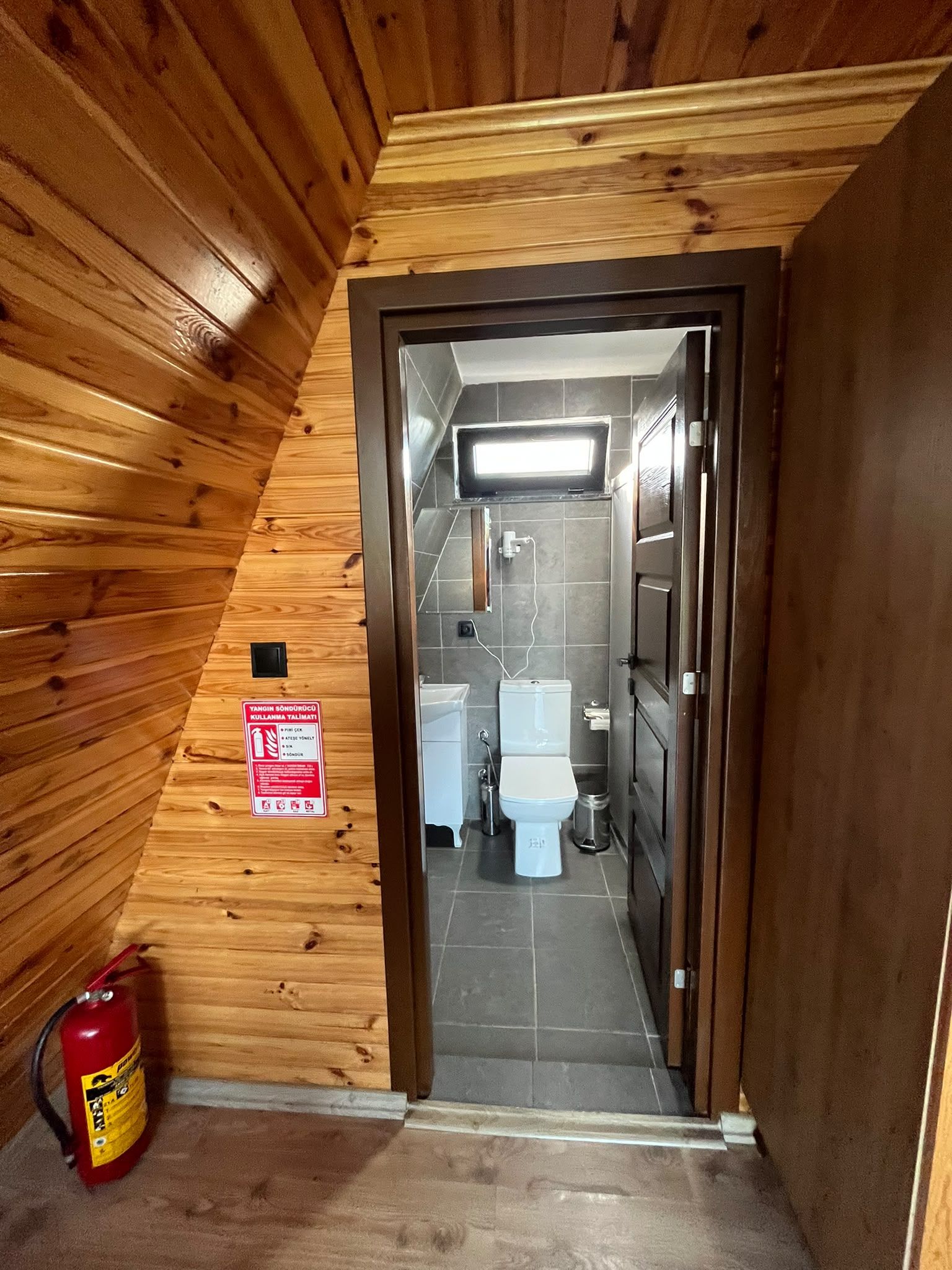 A wooden interior with a door leading to a bathroom containing a toilet and a sink.