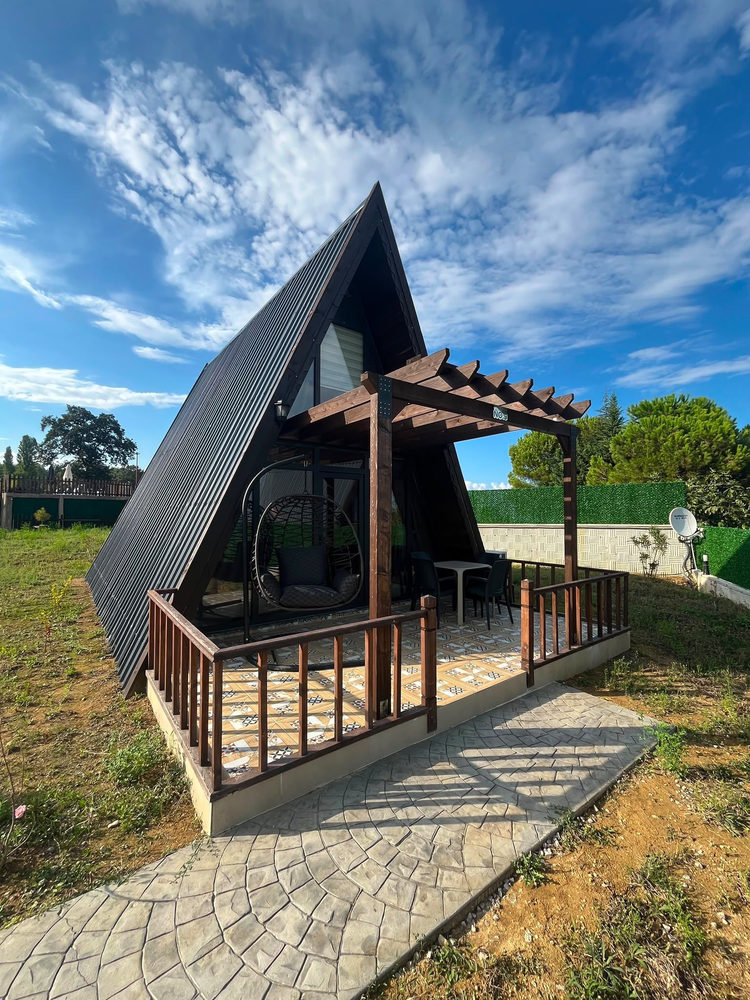 Un edificio moderno de forma triangular con una pérgola de madera y un patio con tejas.