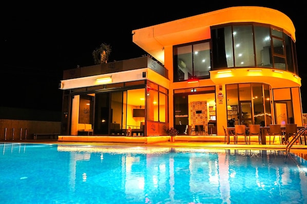 Un hotel moderno con piscina, ventanas amplias y mobiliario exterior.