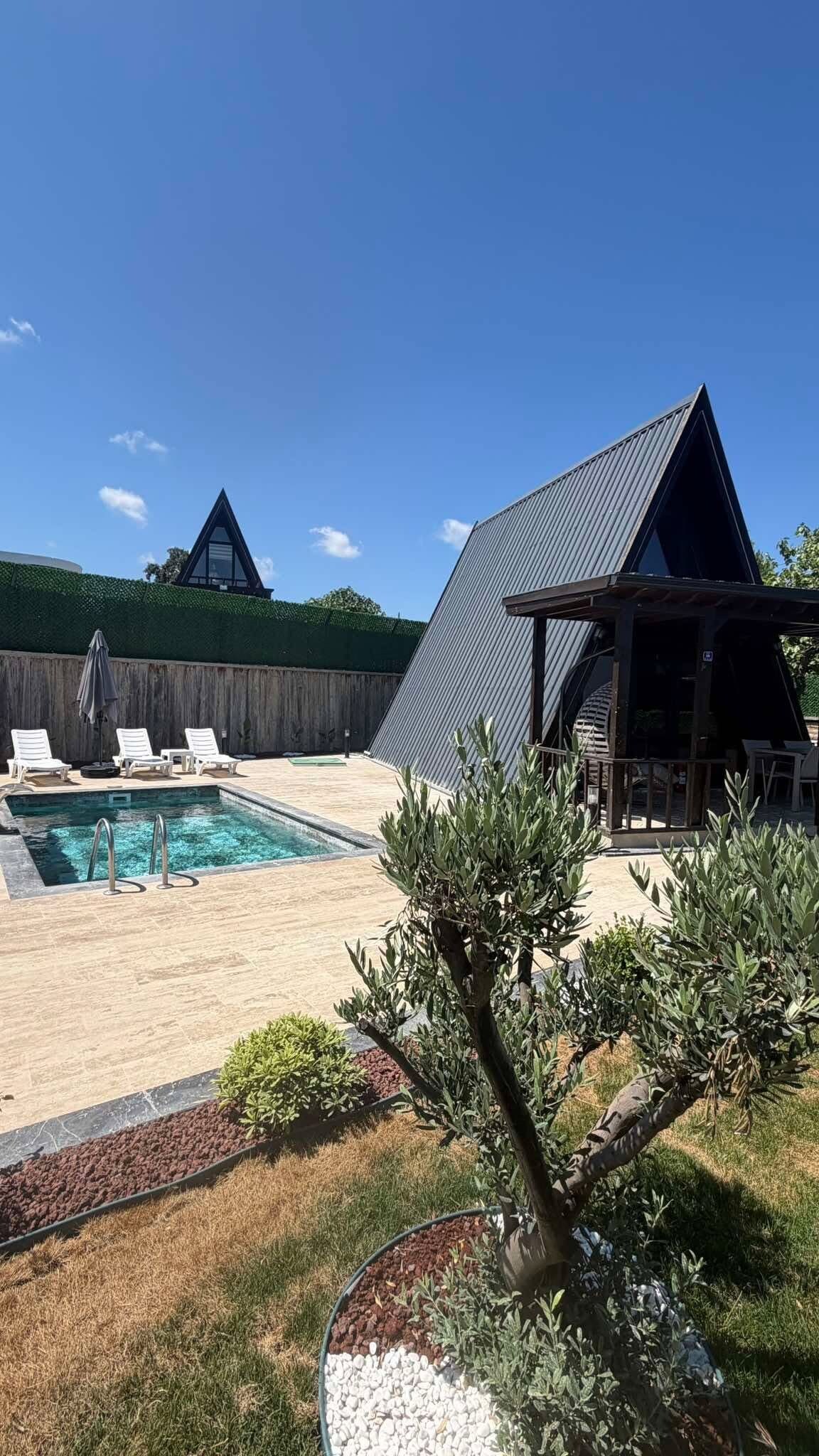 Un patio trasero con piscina, sillas de descanso, una pérgola y una zona vallada.