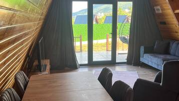 Een knus vertrek met een houten tafel en stoelen, een bank en een groot raam met gordijnen.