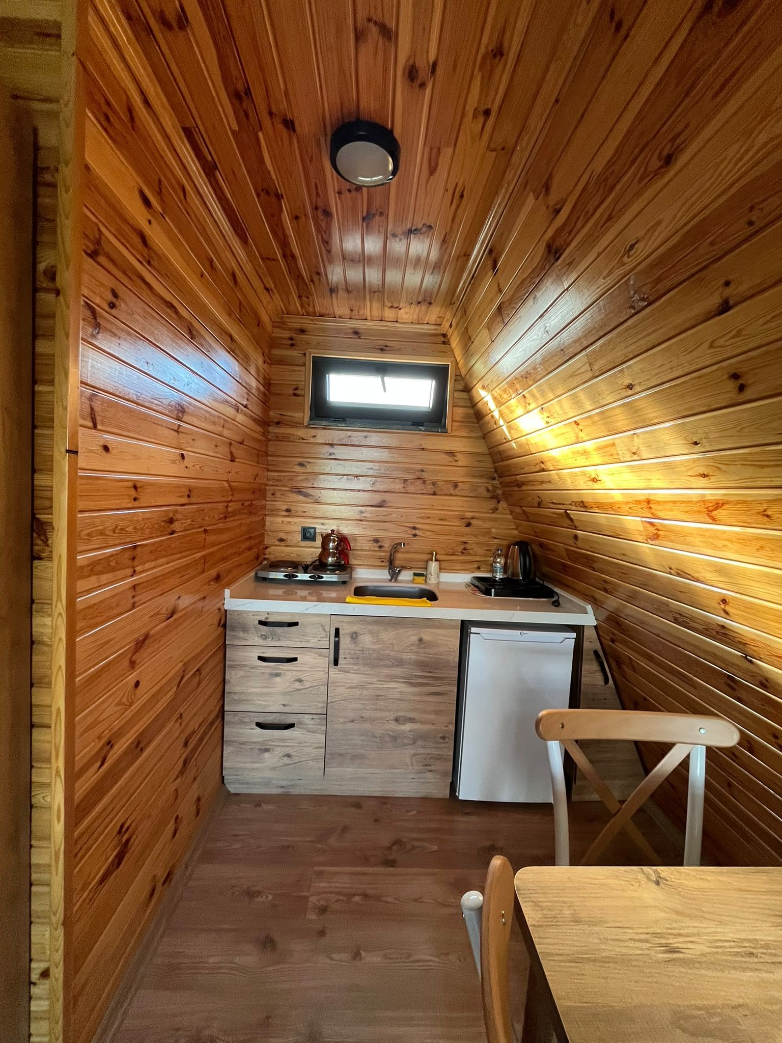 Una cocina compacta con paredes de madera, un ventanal pequeño, un lavamanos, una estufa y un refrigerador.