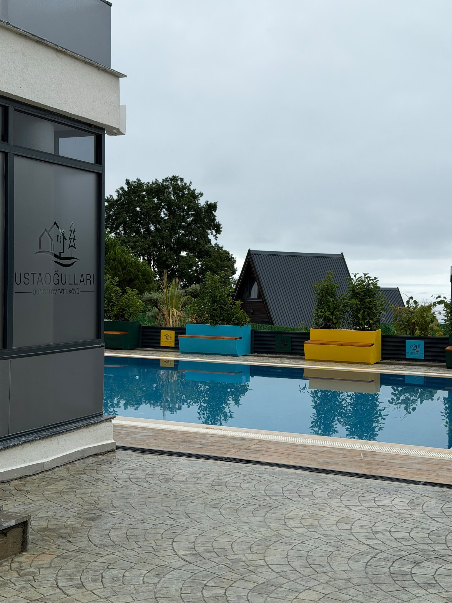 A modern building with a pool, surrounded by greenery and a clear sky.