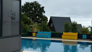 A modern building with a pool, surrounded by greenery and a clear sky.