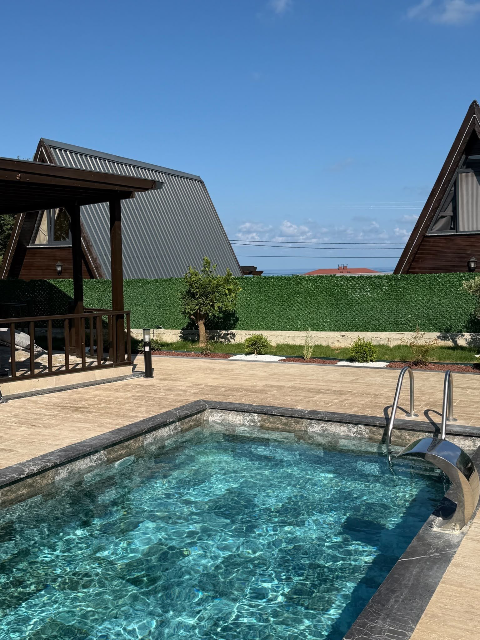 Una piscina con agua cristalina, rodeada por un muelle de madera y una valla metálica.