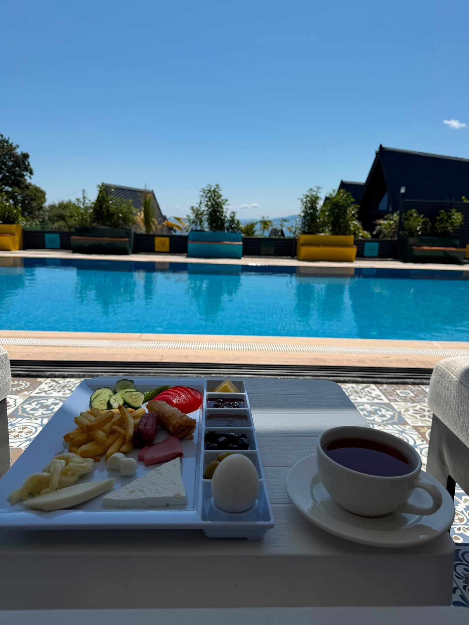 A tray with food and a cup of coffee by a poolside.