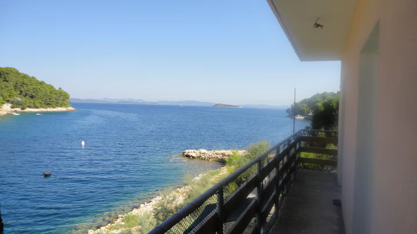 A balcony with a view of a calm sea and distant land.
