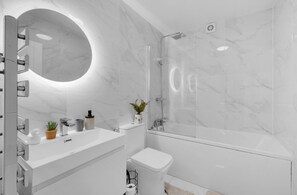 A modern bathroom with a marble floor, a round mirror, a bathtub, and a toilet. - Apartment Sleeps 7 With Wifi (London)