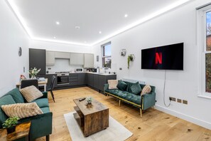 A modern living room with a green sofa, a coffee table, and a TV mounted on the wall. - Apartment Sleeps 7 With Wifi (London)