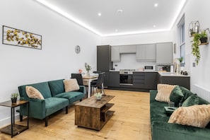 A modern living room with a green sofa, a wooden coffee table, and a dining area with a white table and chairs. - Apartment Sleeps 7 With Wifi (London)