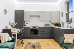 A modern kitchen with a dining area, featuring a built-in oven, microwave, and a coffee machine. - Apartment Sleeps 7 With Wifi (London)