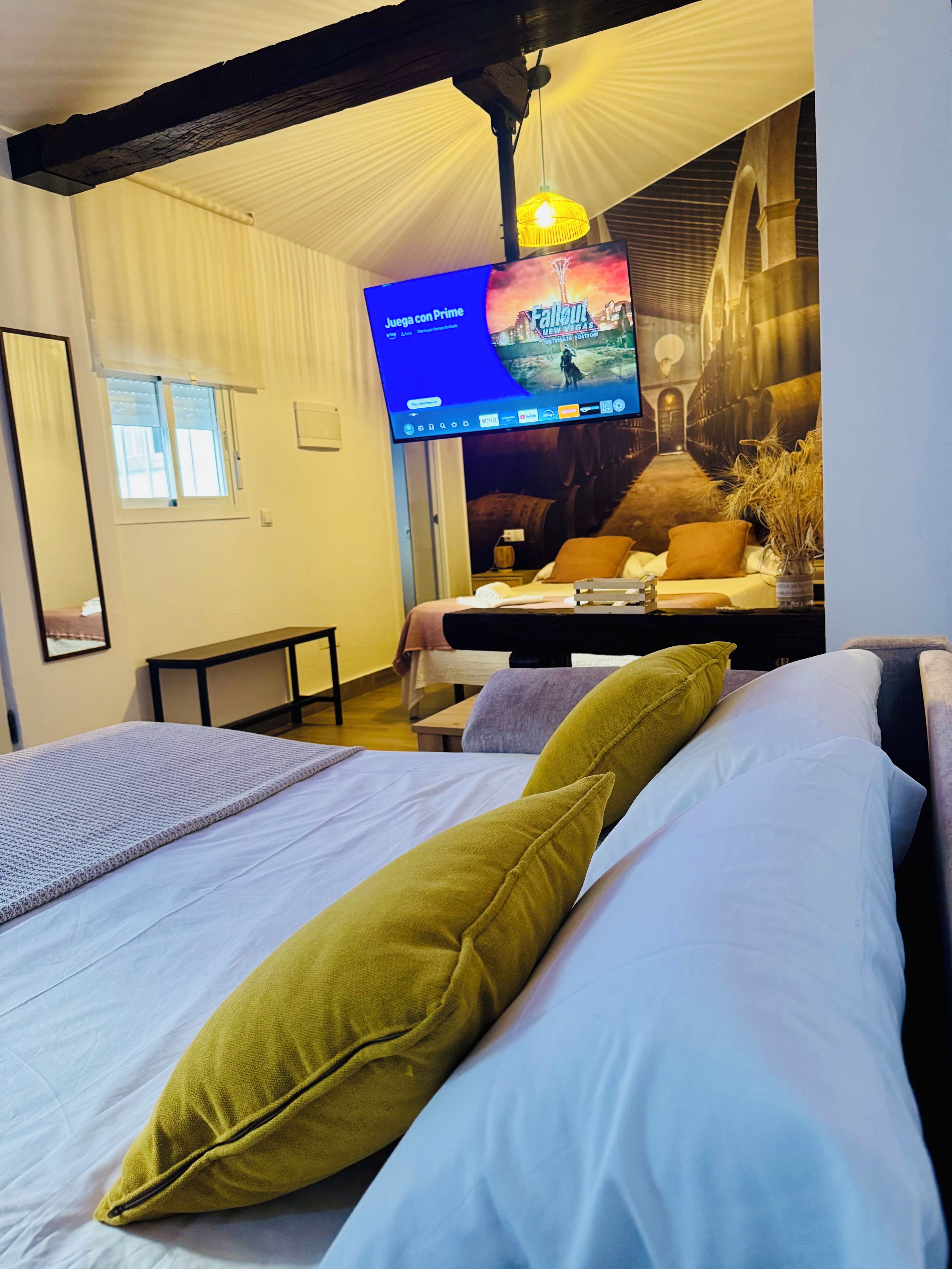 Una habitació d'hotel amb un llit, una taula de treball, una televisió que mostra un joc i un mural a la paret.
