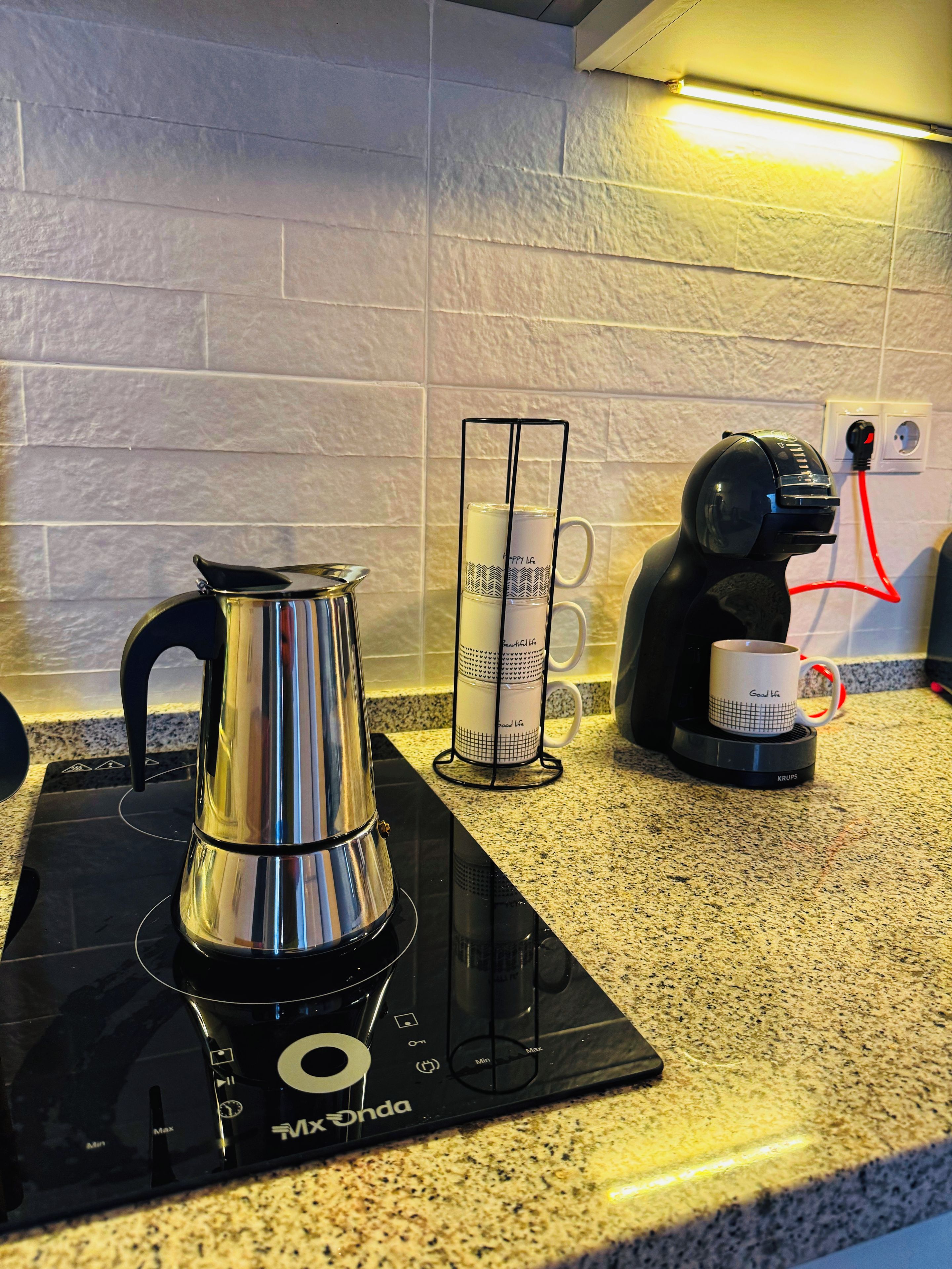 Una cucina con piano cottura a induzione nero, bollitore in acciaio inossidabile, port tazze e macchina per il caffè.