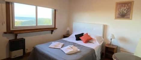 A bedroom with a bed, a chair, a desk, a ceiling fan, and a window.