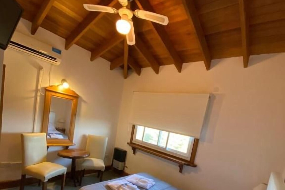 Un dormitorio con cama, escritorio, silla, ventilador de techo y ventana.