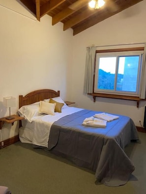 Un dormitorio con cama, mesita de noche, ventana con cortinas y vistas al exterior.