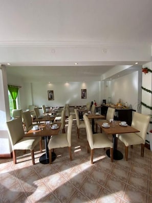 Un comedor con varias mesas y sillas, dispuesto en un espacio amplio.