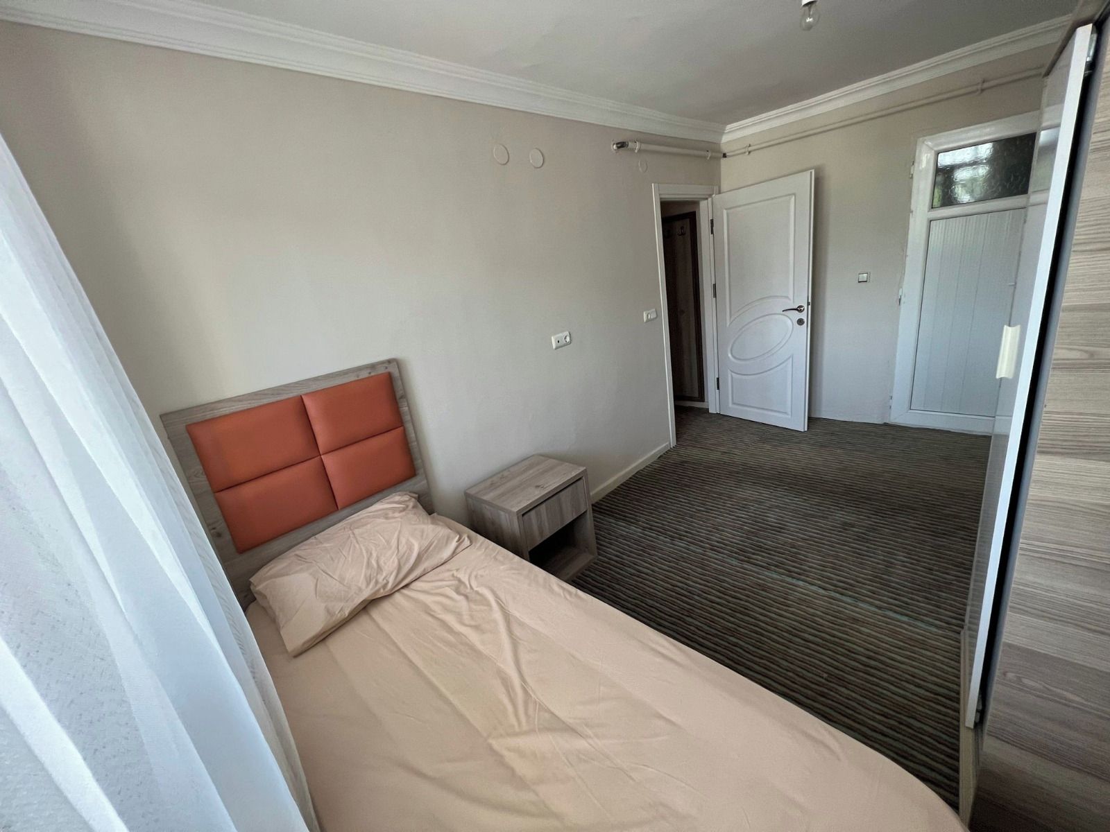 Una camera d'albergo con un letto, un comodino, una porta e un pavimento tappezzato.