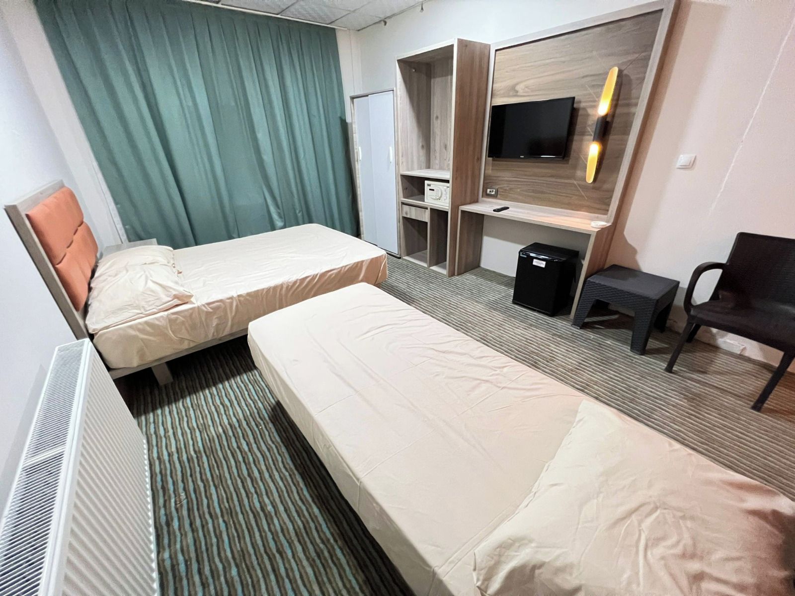 A hotel room with two beds, a desk, a television, a chair, and a small trash bin.