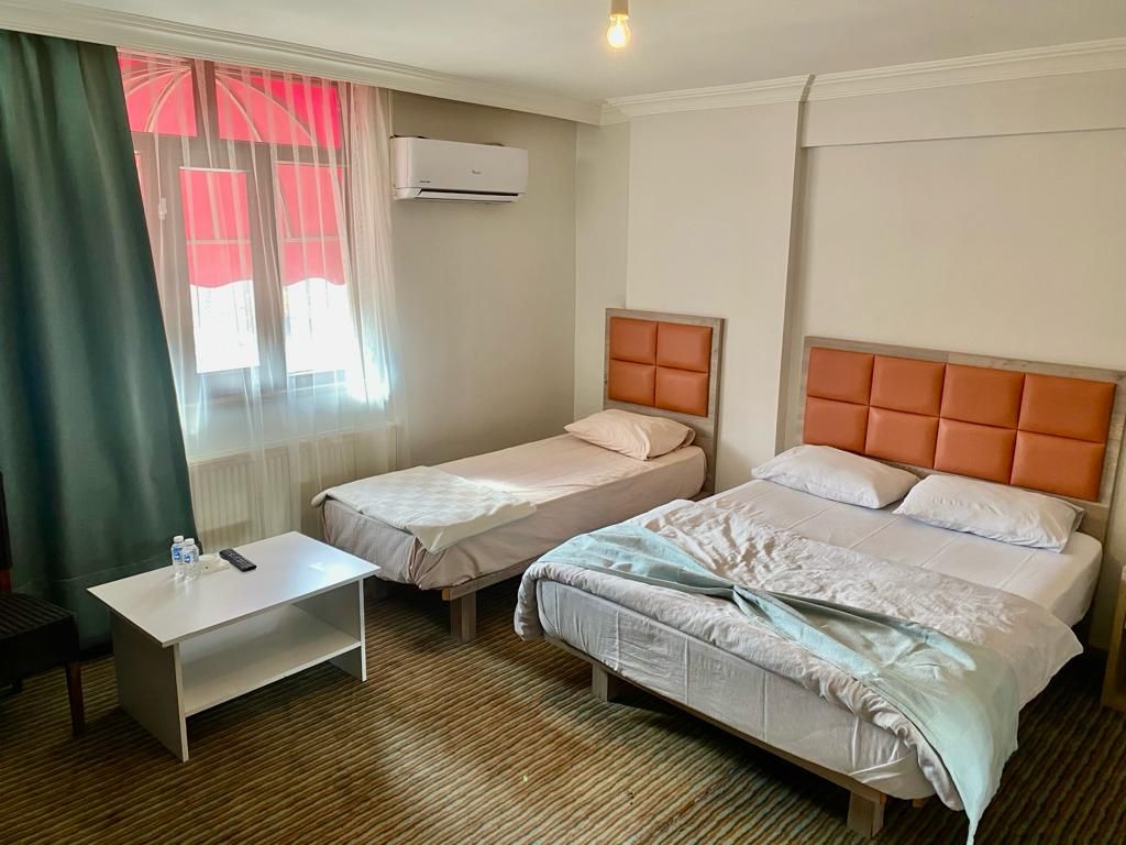 Une chambre d’hôtel avec deux lits, une petite table et une fenêtre avec des rideaux.
