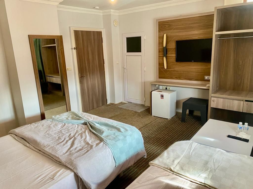 A hotel room with two beds, a desk, a small refrigerator, and a TV mounted on the wall.