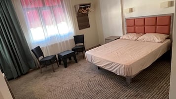 Een hotelkamer met een bed, een bureau, twee stoelen, een raam met gordijnen en een wandlamp.