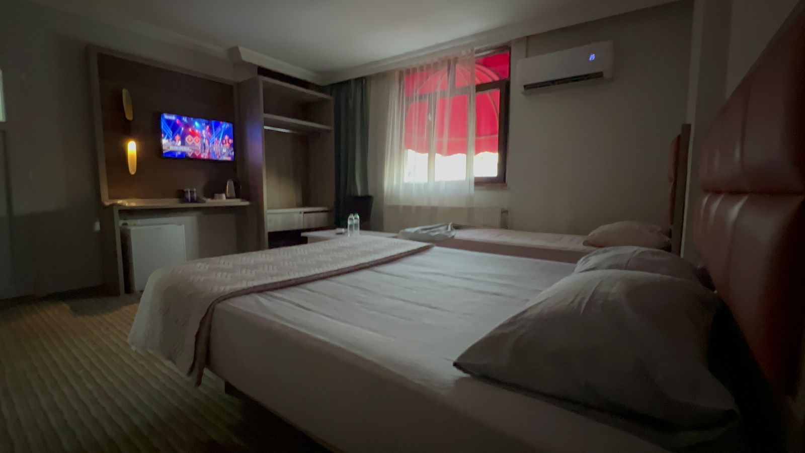 Quarto de hotel com cama, televisão, escrivaninha e janela com cortinas.