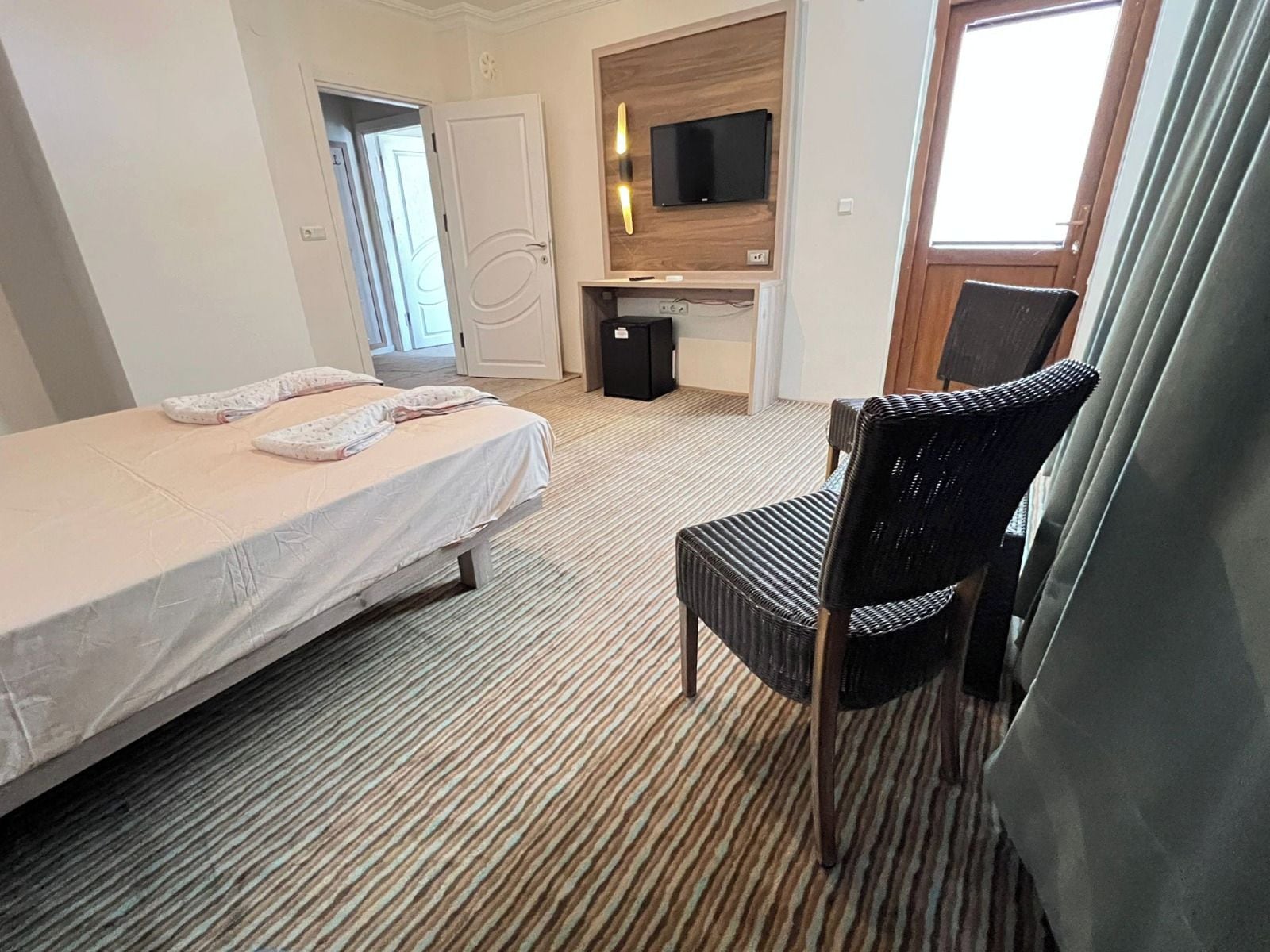 Habitación de hotel con cama, una silla, escritorio y televisor, además de una puerta.