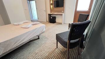 Habitación de hotel con cama, una silla, escritorio y televisor, además de una puerta.