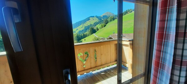 A wooden balcony with a view of green hills and a clear sky.