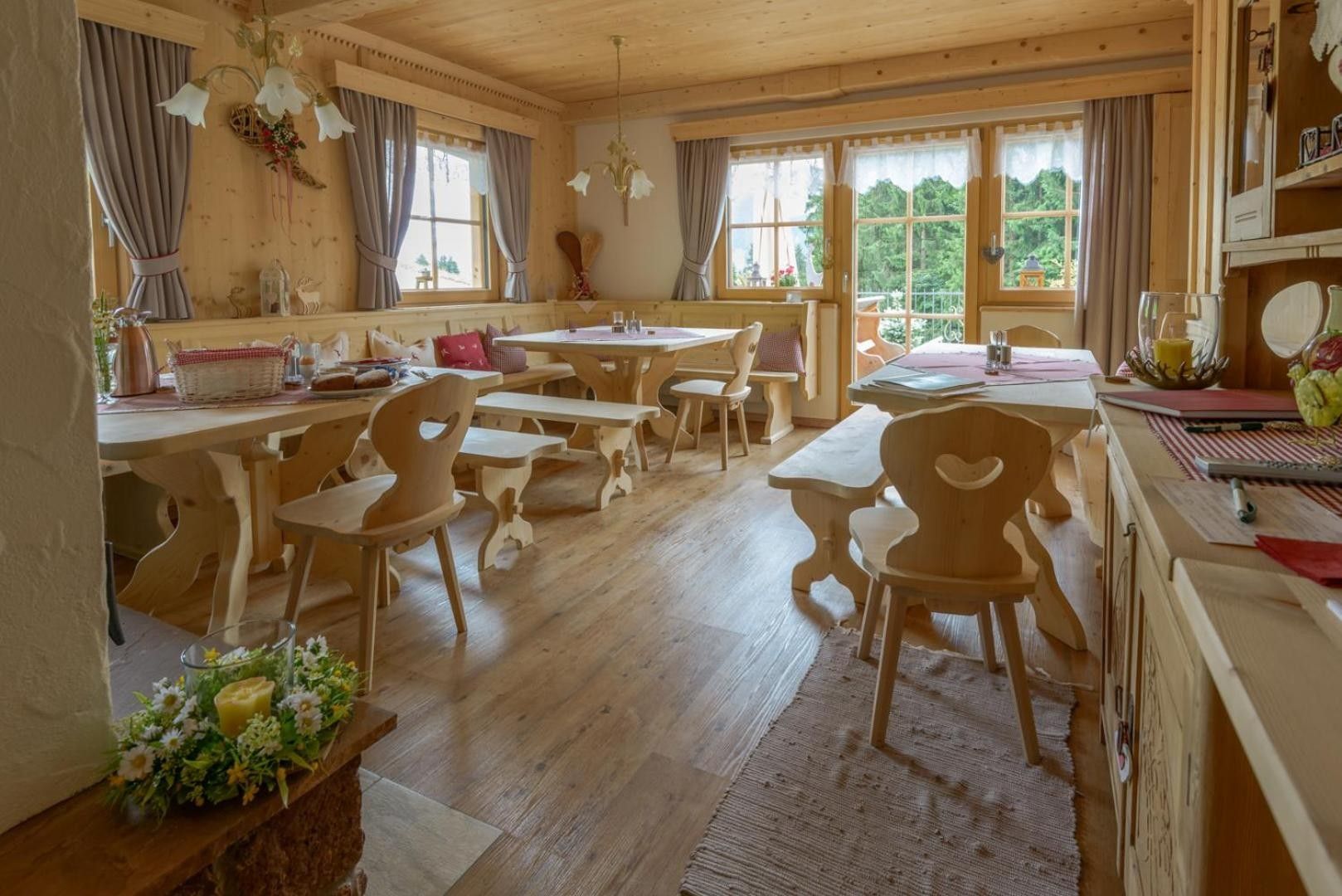 A wooden interior with multiple tables and chairs, large windows, and a chandelier.