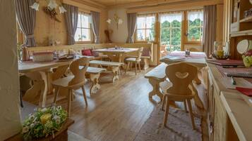 A wooden interior with multiple tables and chairs, large windows, and a chandelier.