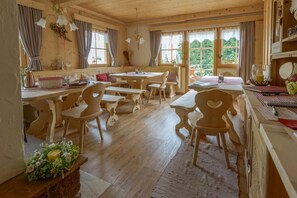 A wooden interior with multiple tables and chairs, large windows, and a chandelier.