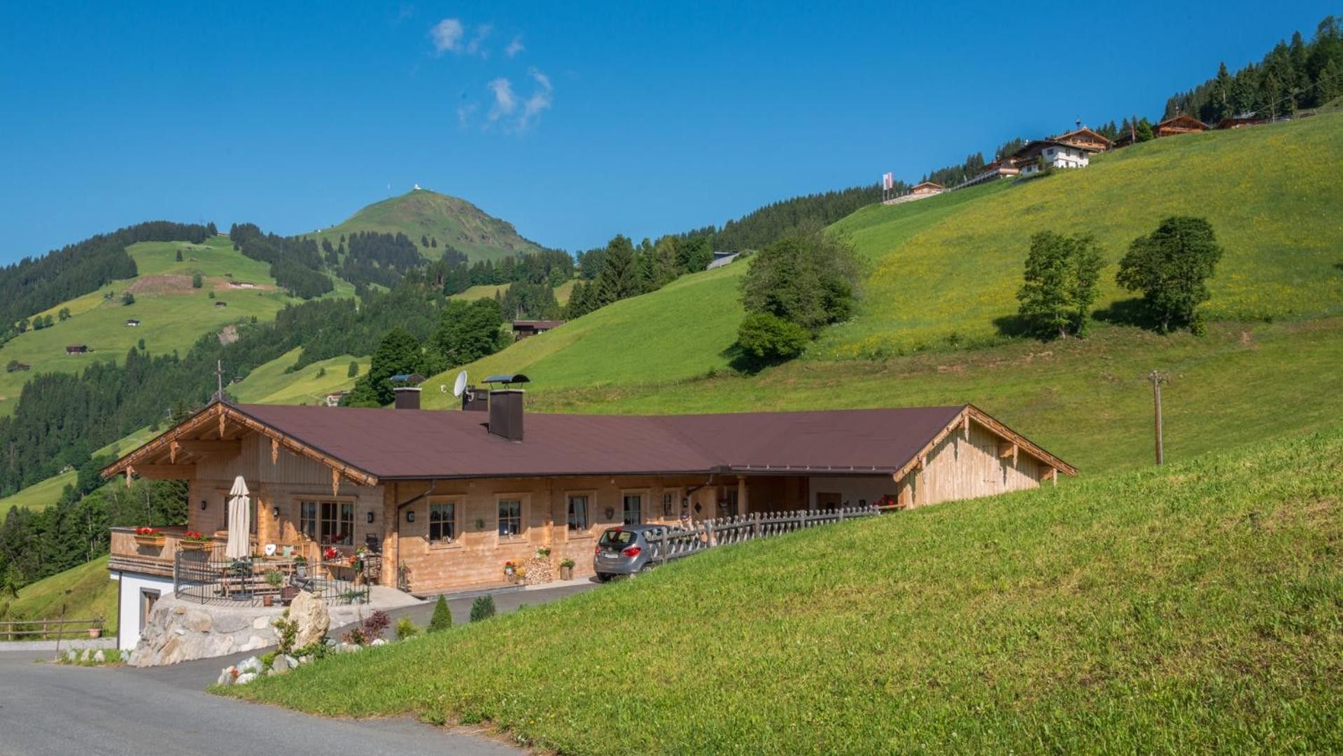 A wooden chalet with a sloped roof, a stone foundation, and a car parked in front.