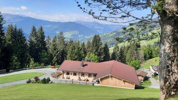 Eine Holzhütte mit rotem Dach, umgeben von üppiger Vegetation und Bergen im Hintergrund.