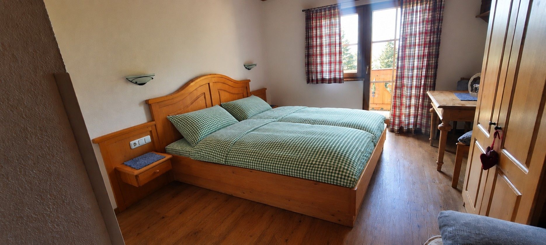 Une pièce avec un lit en bois, un bureau en bois et une fenêtre ornée de rideaux à carreaux.