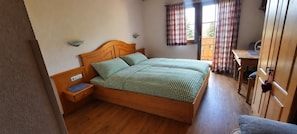 Une pièce avec un lit en bois, un bureau en bois et une fenêtre ornée de rideaux à carreaux.